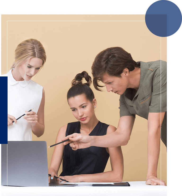 Three people are looking at a laptop while one of them is holding a cell phone.