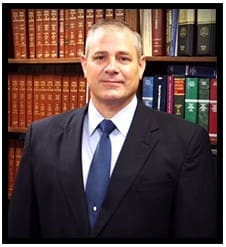 A man in suit and tie standing next to a book shelf.