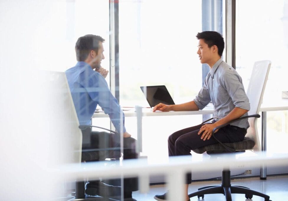 Two men are sitting at a table with laptops.