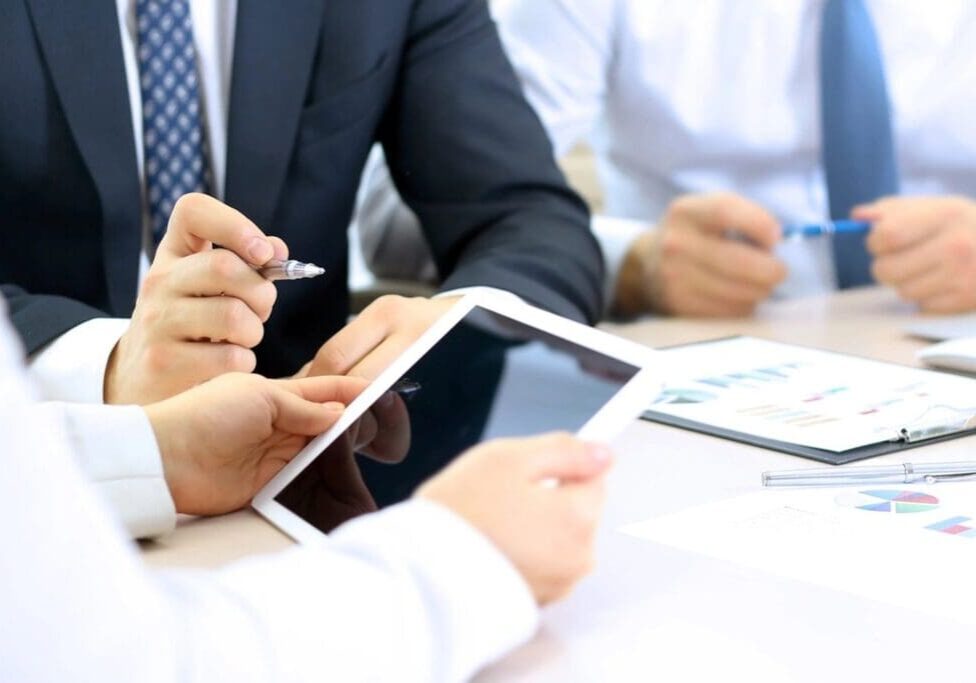 A group of people sitting at a table with papers and a tablet.